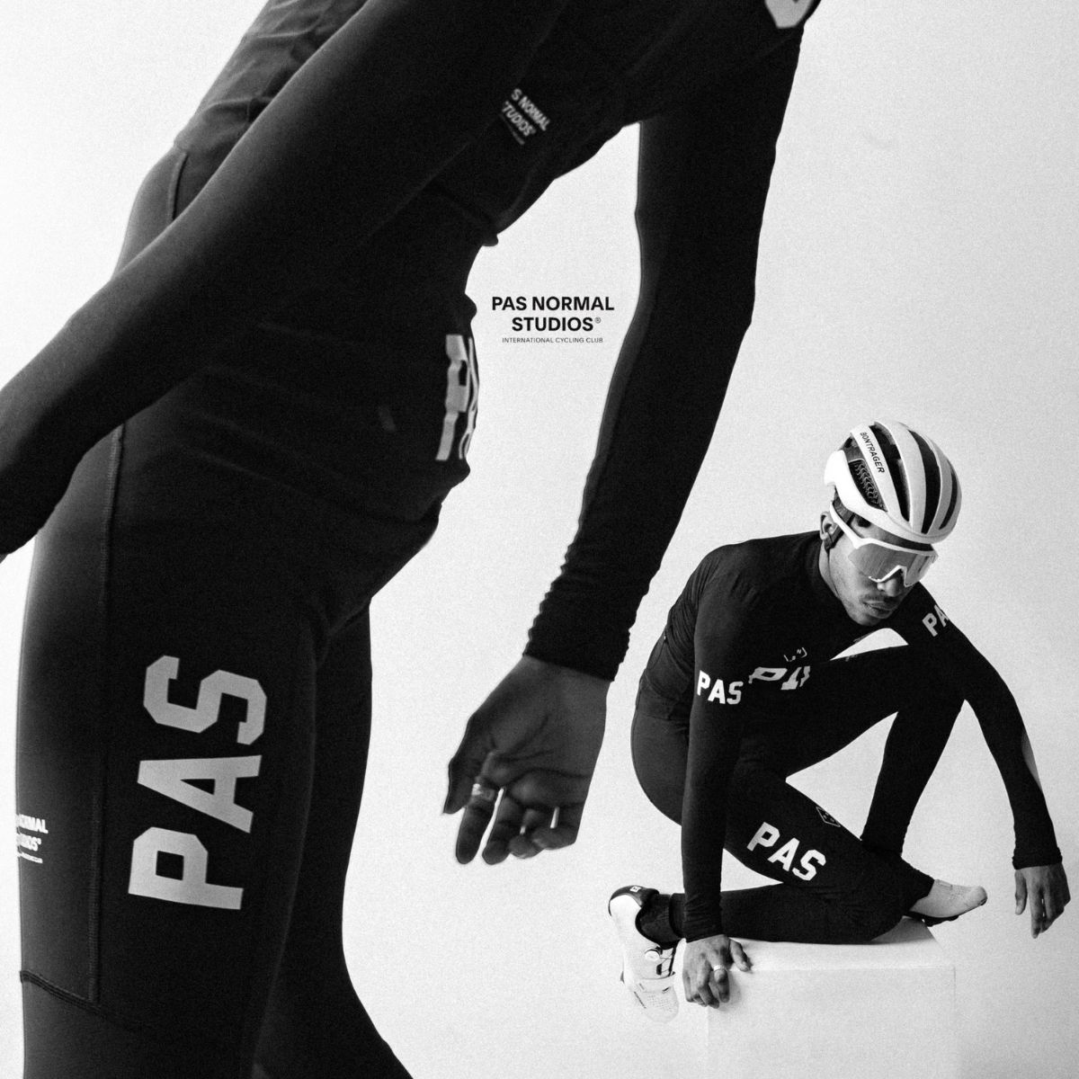 Black and white image of a cyclist wearing PAS Normal Studios gear. The cyclist crouches on a white cube, wearing a helmet and sunglasses. Another part of the image shows a close-up of the cycling apparel from a different angle.