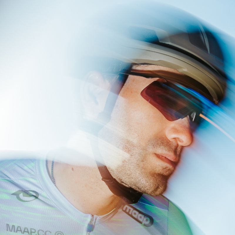 A cyclist wearing a helmet and sunglasses is captured in motion, with a blur effect emphasizing speed.