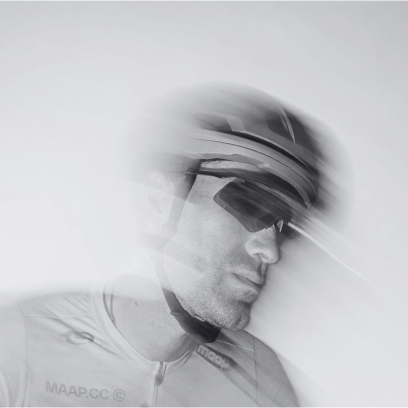 A cyclist wearing a helmet and sunglasses appears blurred, creating a sense of motion in this black-and-white image.
